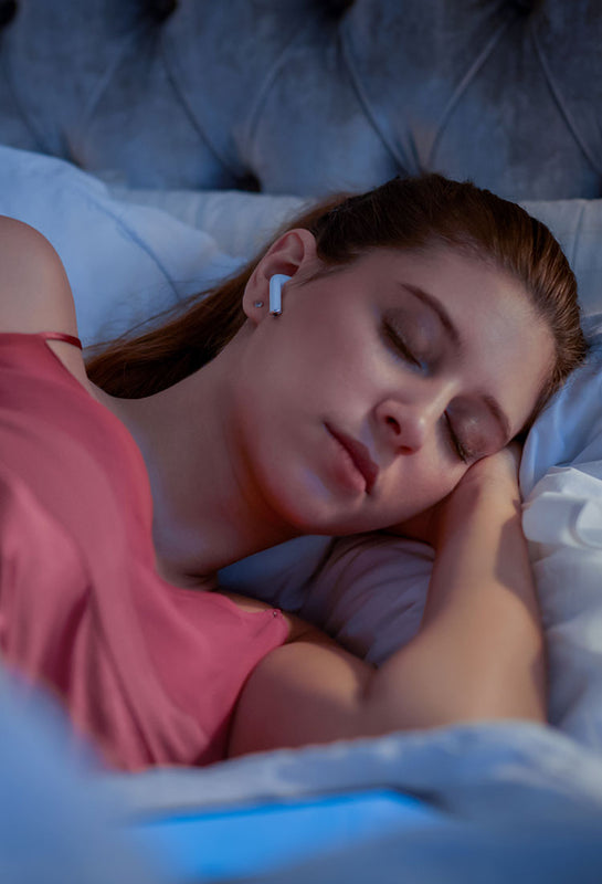 smartsleep sleep Sounds und Podcast Junge Frau liegt mit Kopfhörern im Bett und hört Musik und Geräusche der sleep TUNES und sleep NOISES um entspannt einzuschlafen